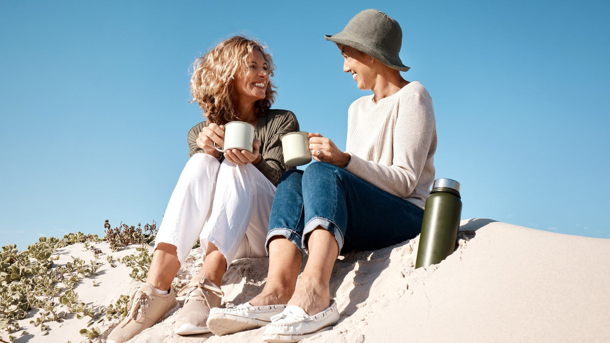Two women in their fifties sitting on a dune with mugs, illustrating collagen support through menopause